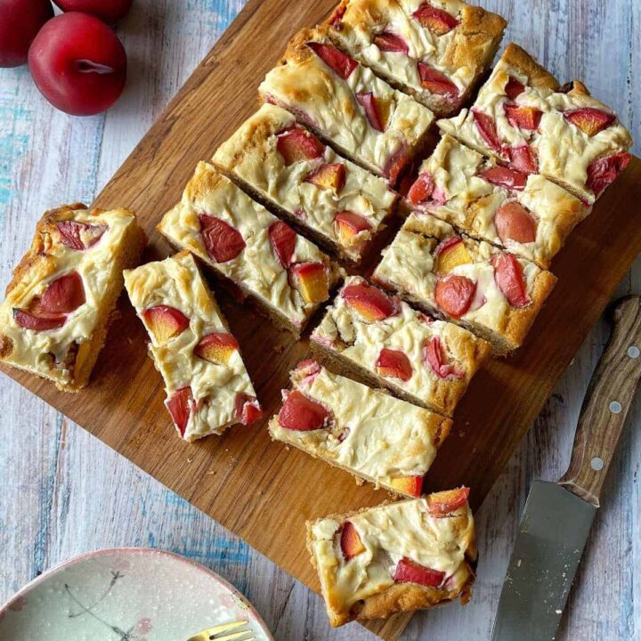 Cooked and sliced plum and cream cheese tray bake on a wooden chopping board.