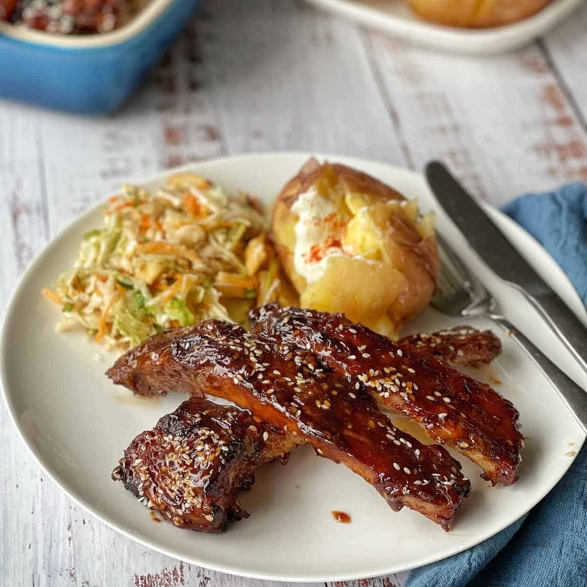 Pork ribs, a baked potato and coleslaw on a white plate. 