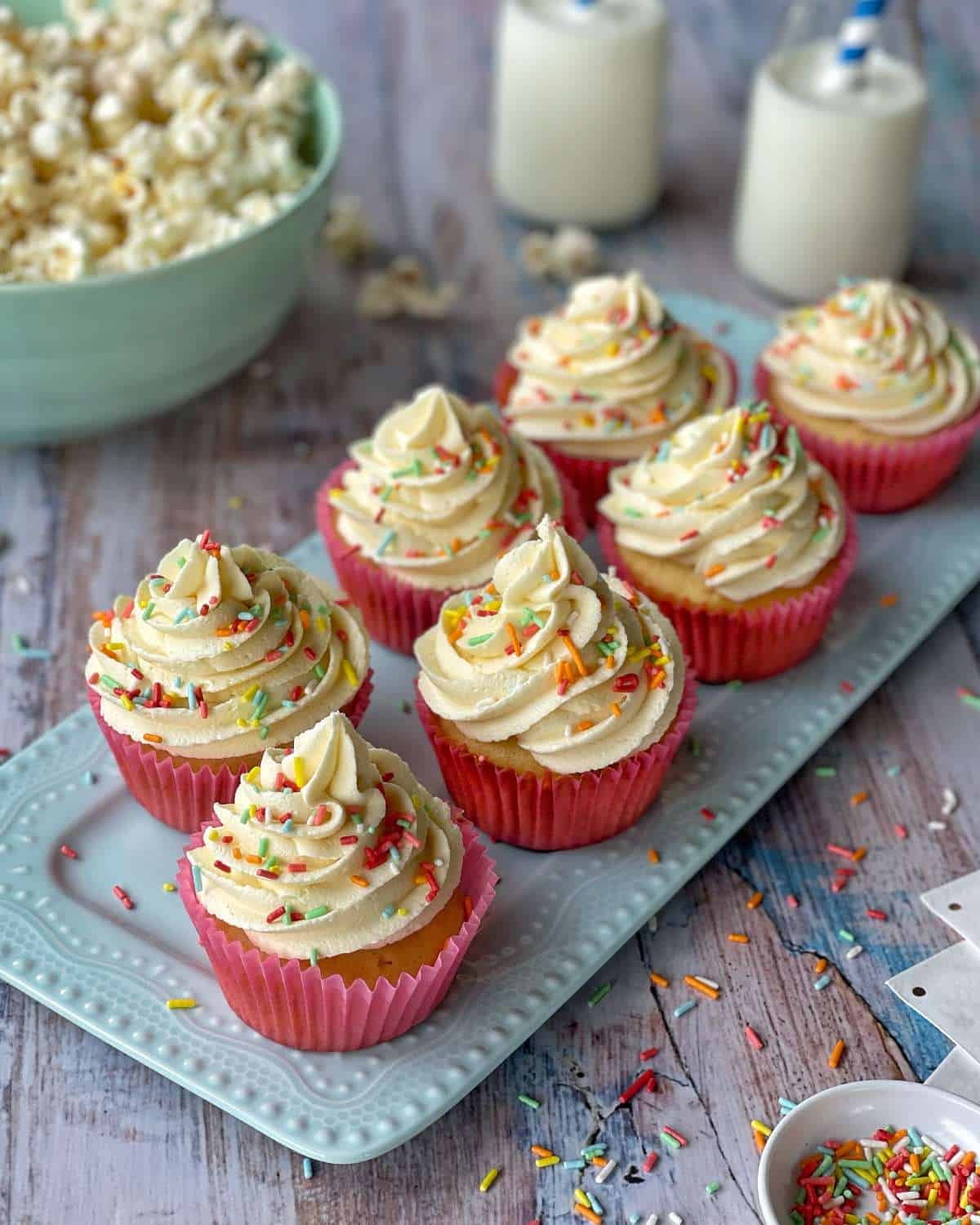 A close up shot of classic vanilla cupcakes with creamy butter icing and colourful sprinkles on top.