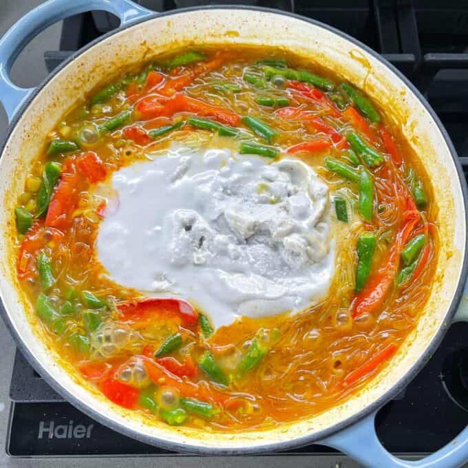 The broth, rice noodles and fresh vegetables for Yellow Fish Curry cooking on a stovetop.