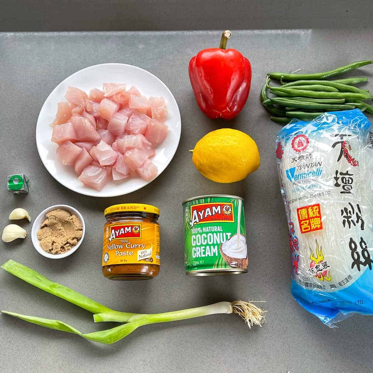 The ingredients for yellow fish curry with rice noodles on a grey bench top.