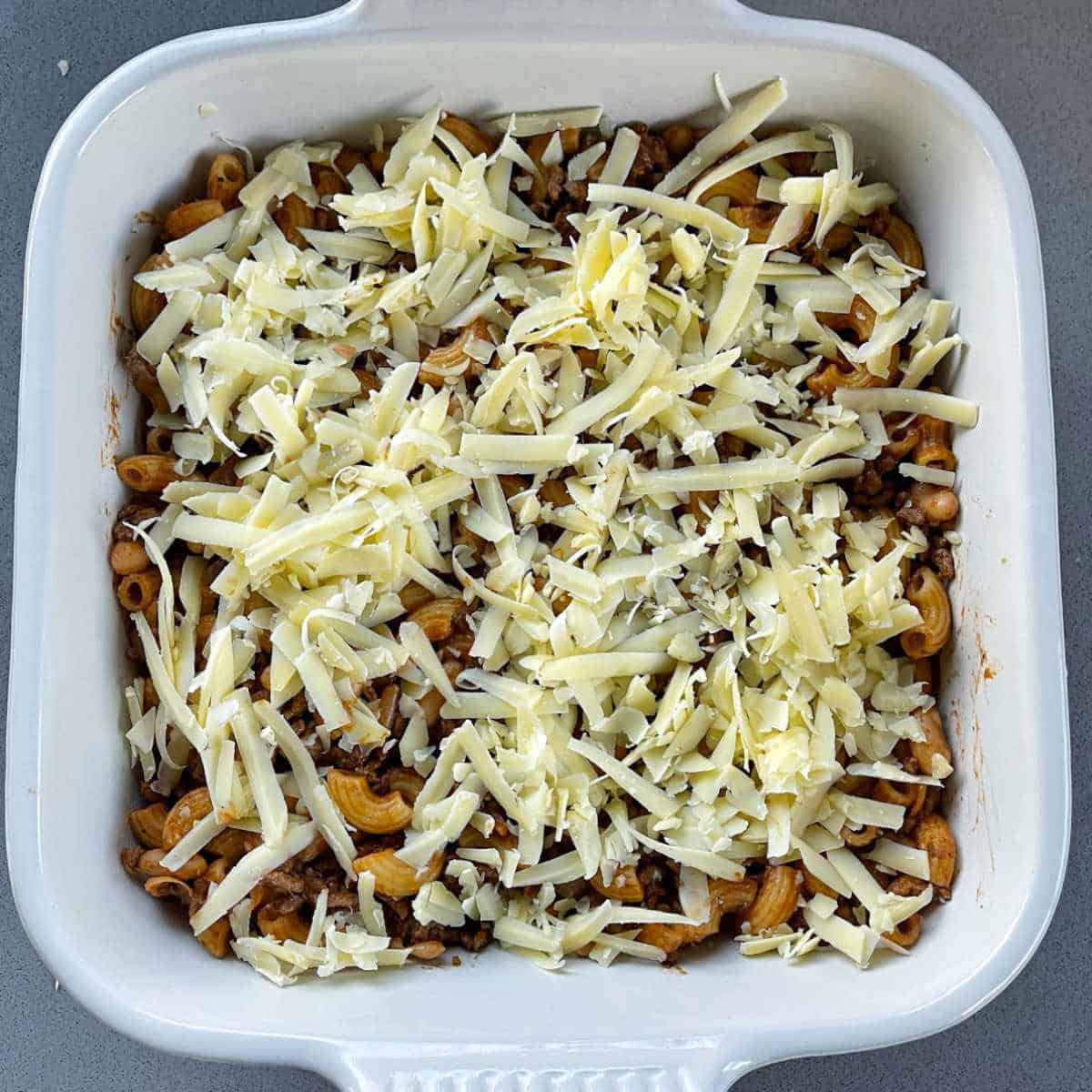 Grated cheese on top of a mince, macaroni and bean casserole prior to being cooked.