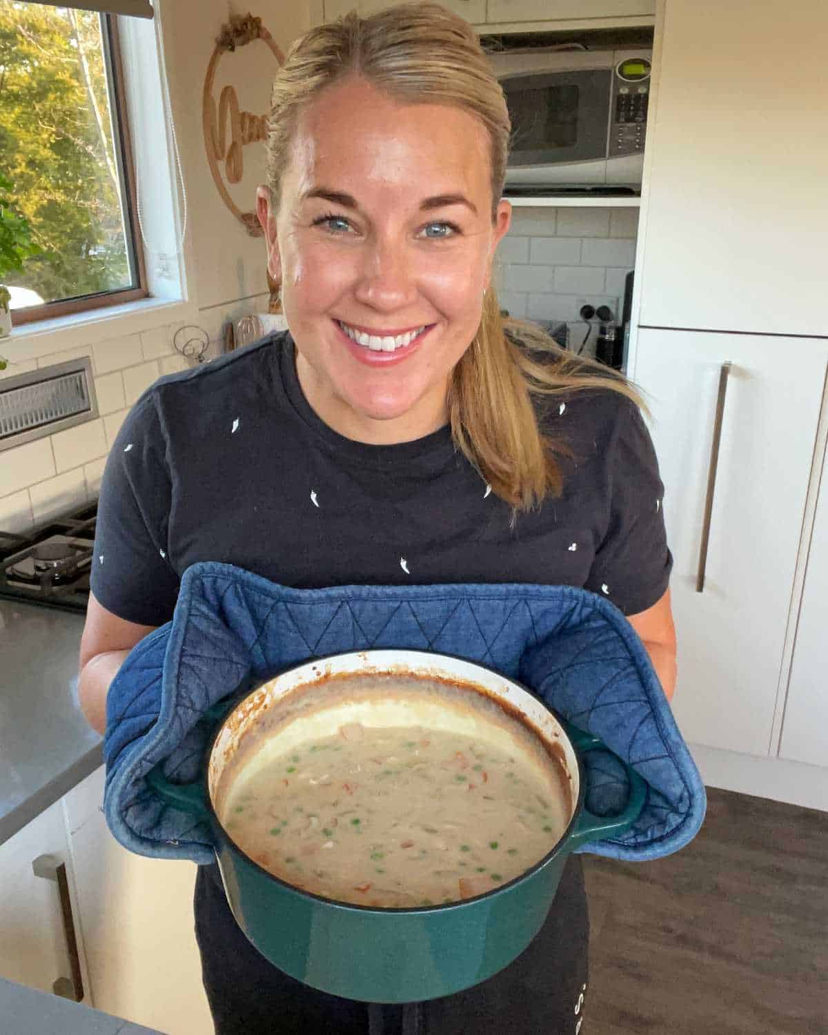 A blonde haired woman holding cooked chicken casserole smiling.