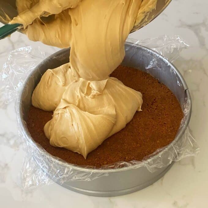 The cream cheese and biscoff filling being poured onto the set base of the cheesecake in a lined cake tin.