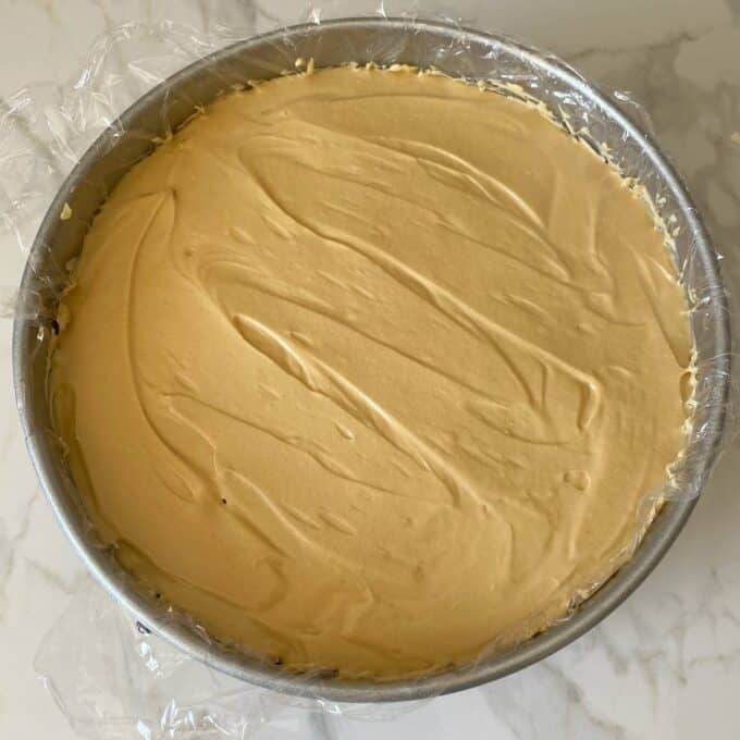 An assembled Biscoff Cheesecake before it has been set in a lined cake tin on a marble bench.