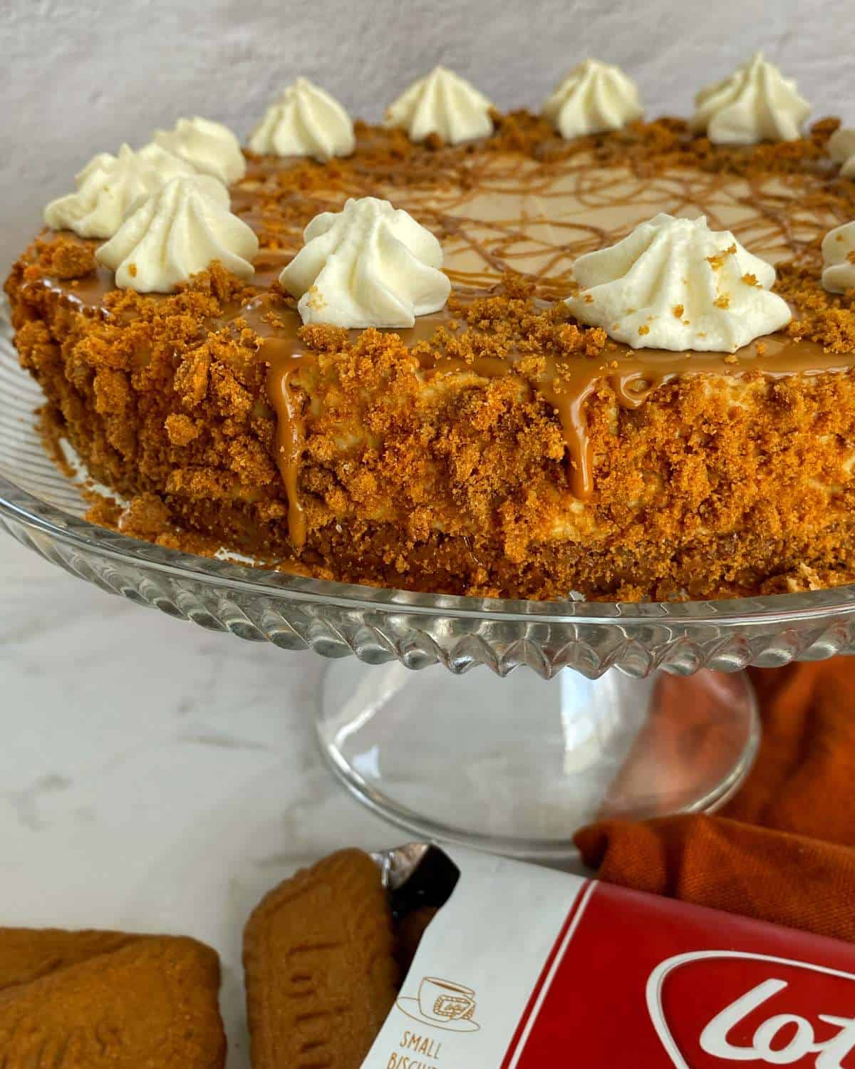 The set Biscoff Cheesecake on a glass cake stand in a marble bench top