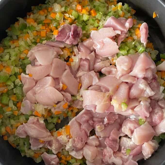 Diced chicken being added to the diced vegetables in a fry pan