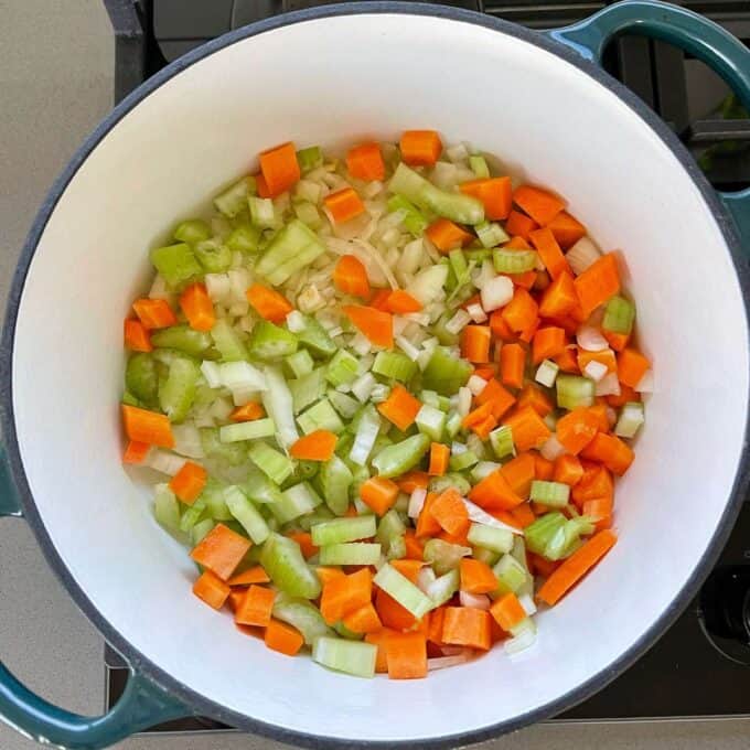 Cubed onion, celery and carrot frying in a medium size ceramic dish over the hob.