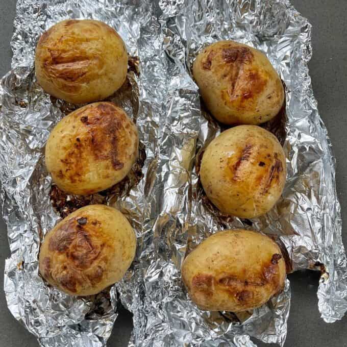 Cooked potatoes that have just been unwrapped from tinfoil sitting on a grey bench top