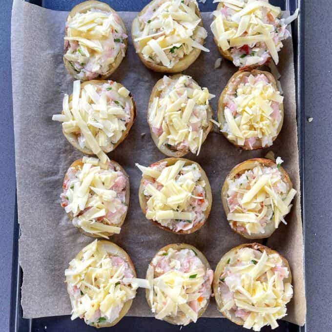 Assembled Jacket Potatoes before being cooked on a lined baking tray.