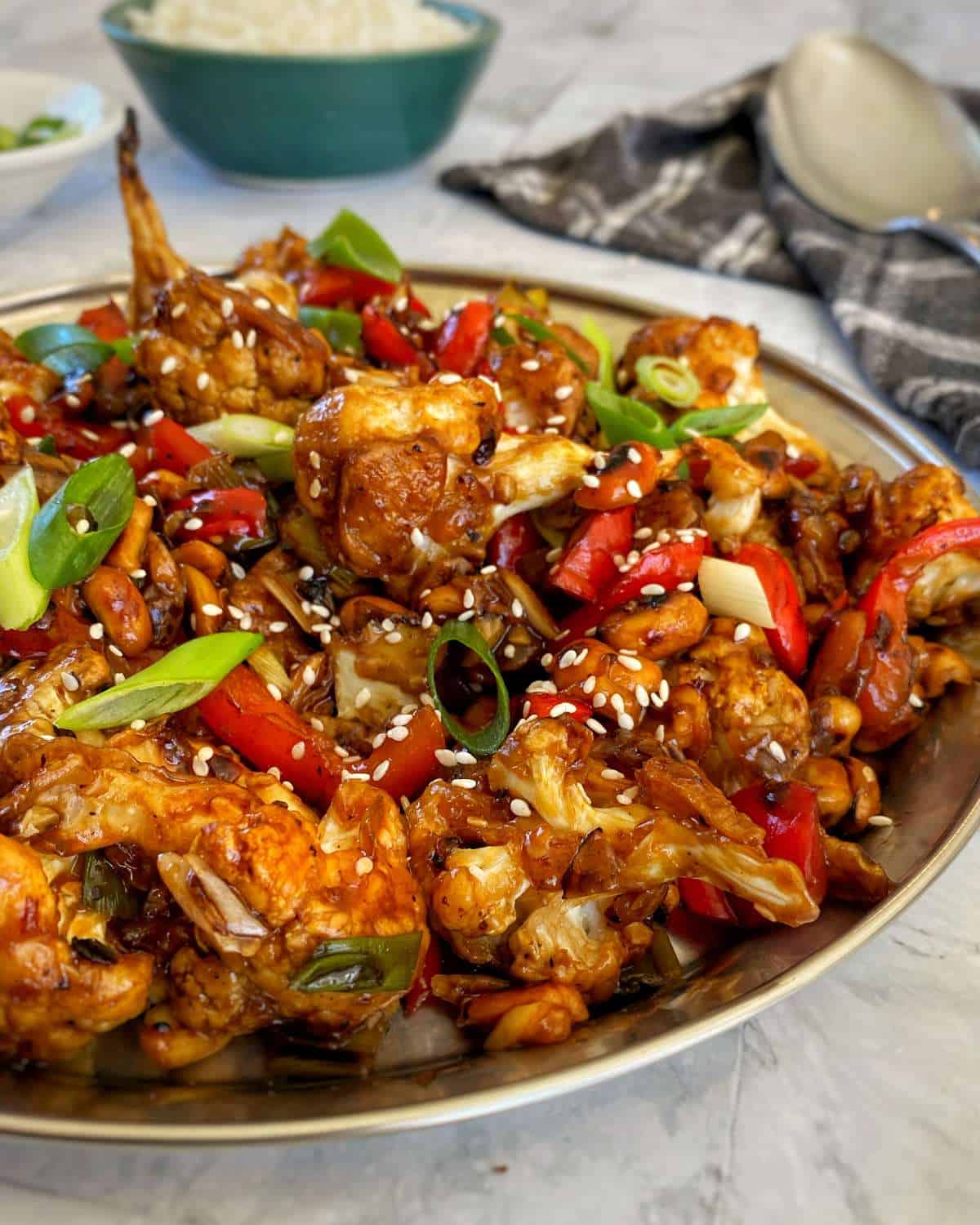 A close up of Kung Pao Cauliflower served in a large bowl with sliced spring onion and sesame seeds scattered over the top.