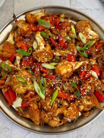 A birds eye view shot of Kung Pao Cauliflower served in a large bowl with sliced spring onion and sesame seeds scattered over the top.