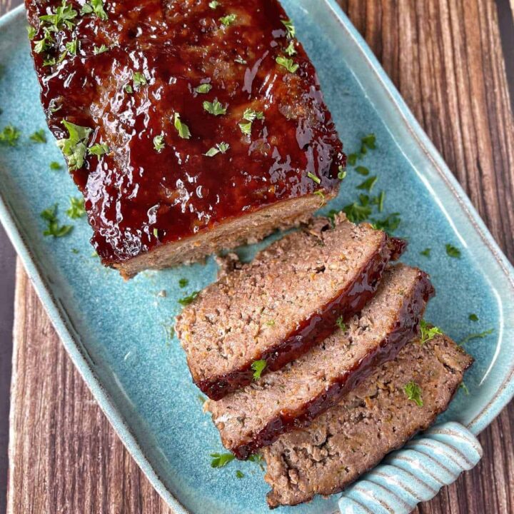 Cooked and sliced Meatloaf served on a dusky blue oval platter, garnished with a sprinkle of parsley.