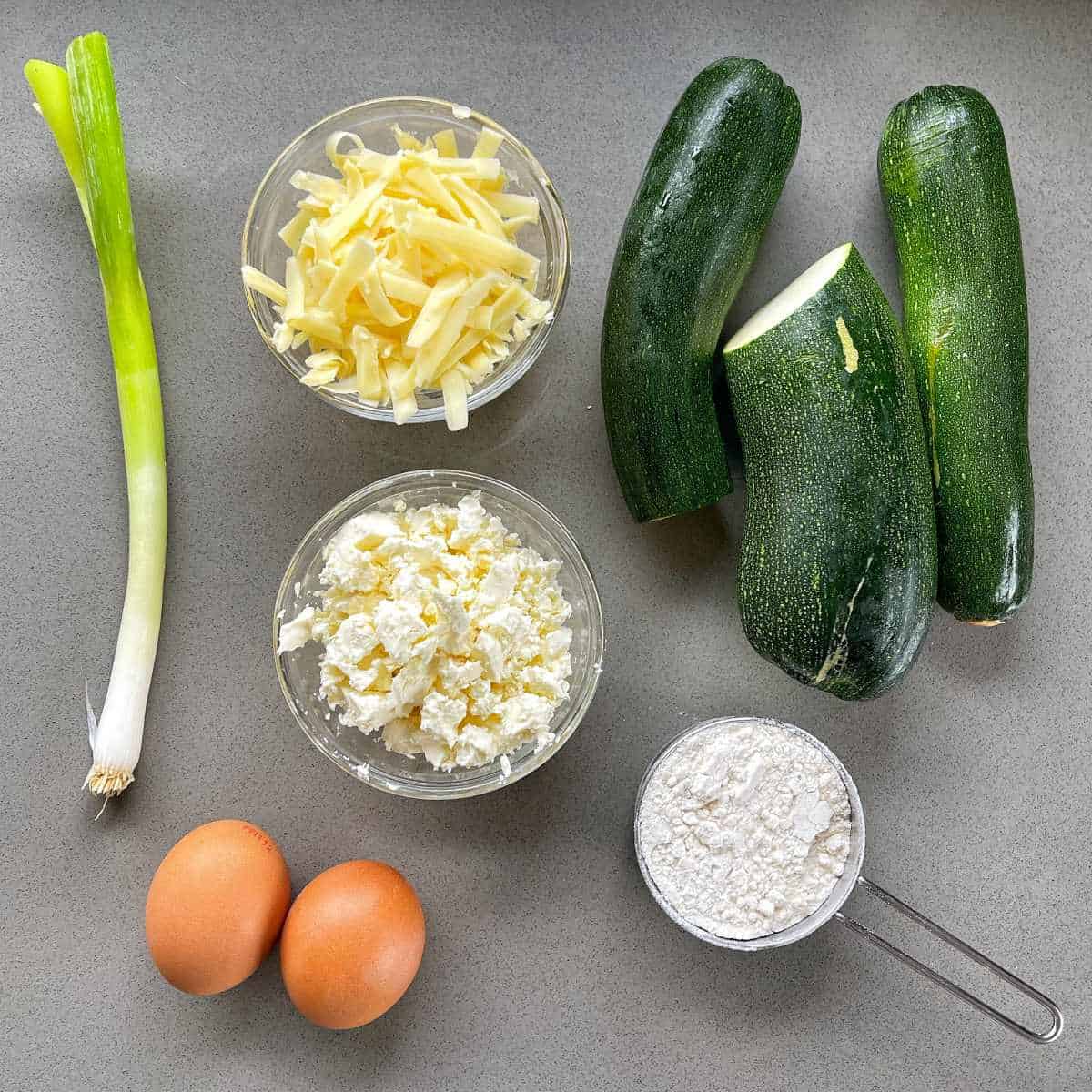 The ingredients for courgette and feta fritters on a grey bench.