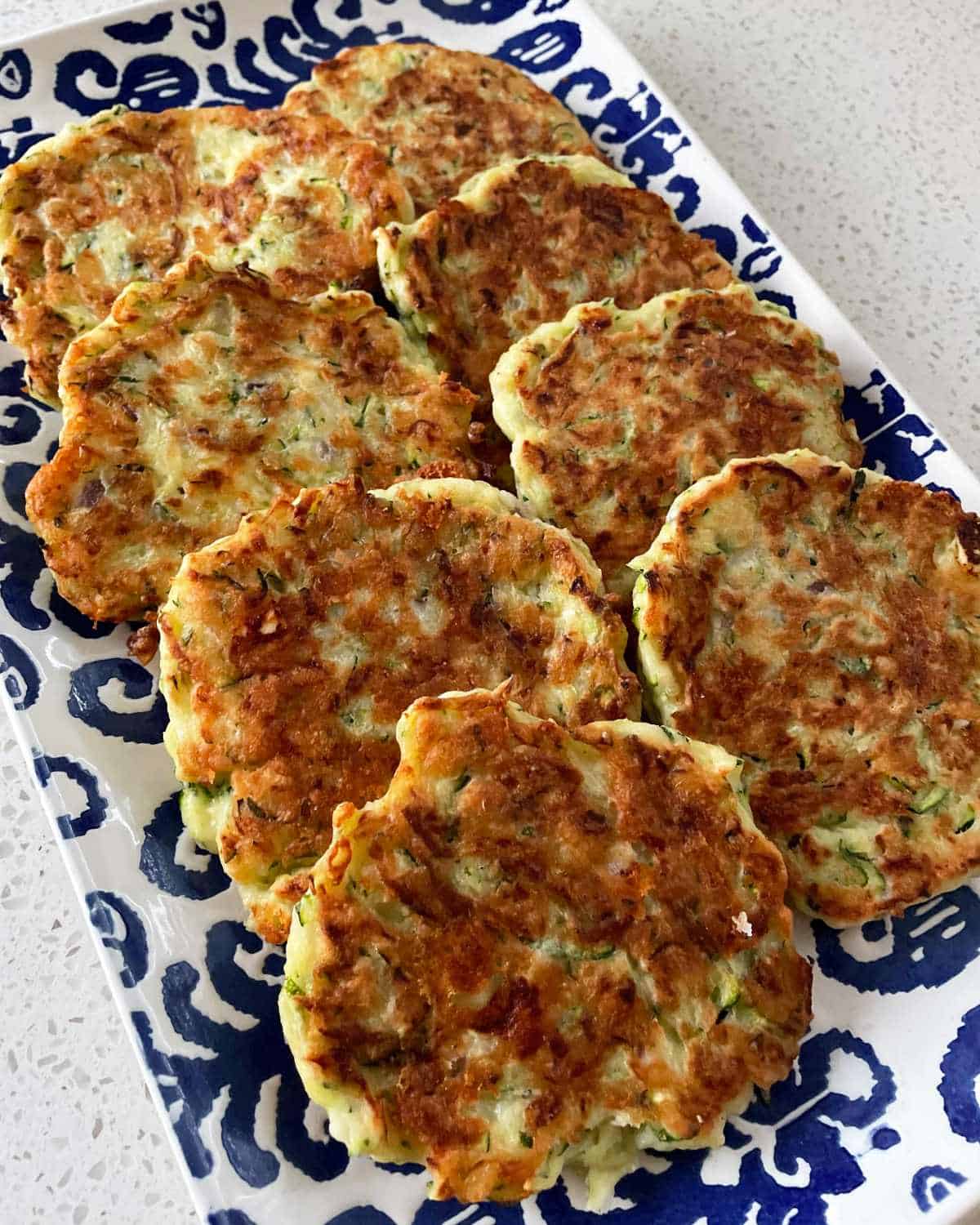 A plate of courgette and feta fritters on a white bench.