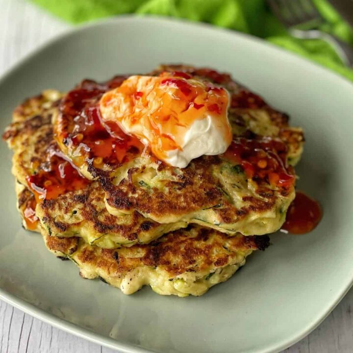 A stack of courgette and feta fritters topped with sour cream and sweet chilli.
