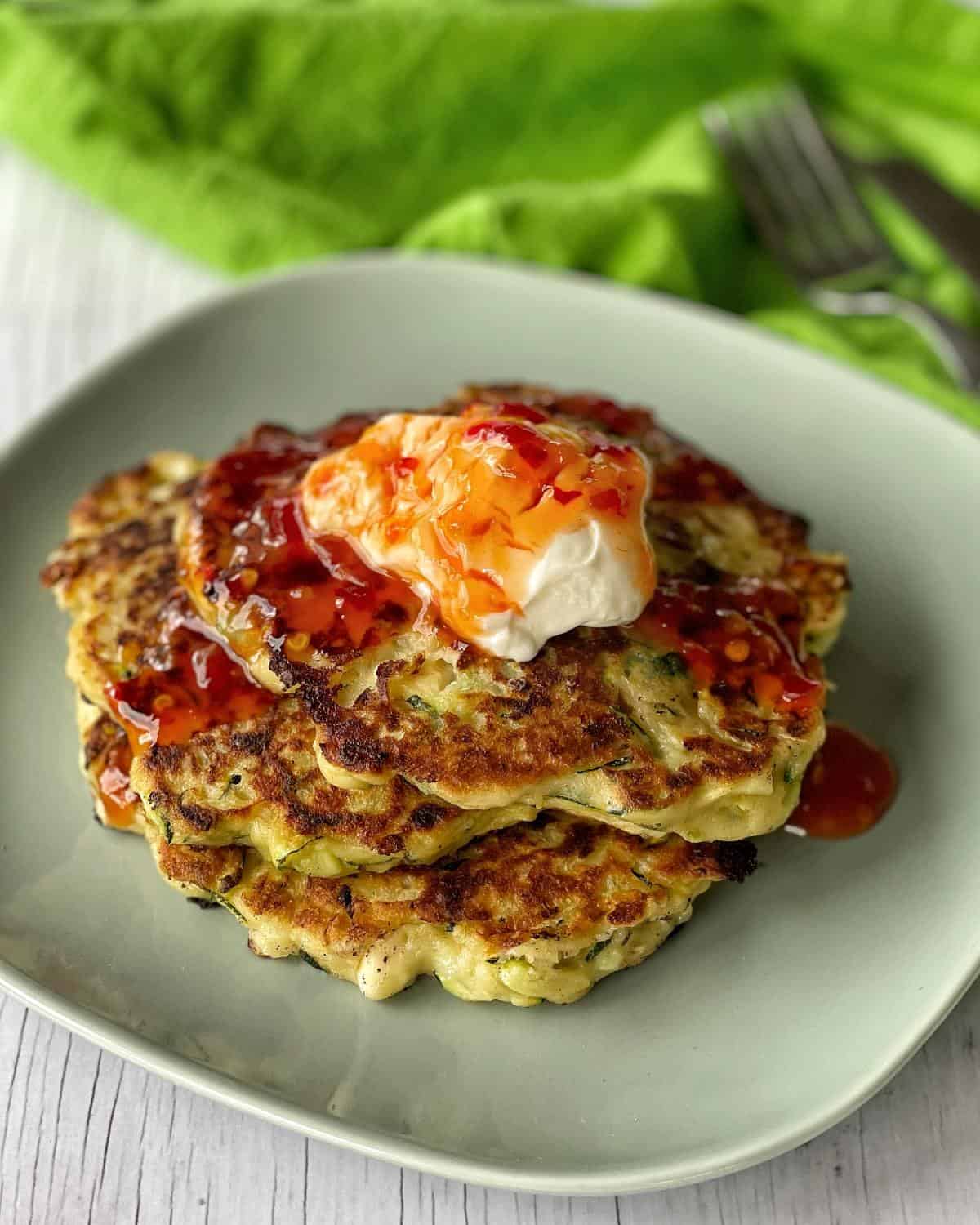 A stack of courgette and feta fritters topped with sour cream and sweet chilli.