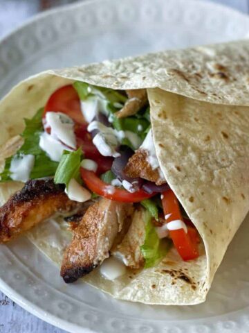A close up of an assembled chicken gyros on a white dinner plate.