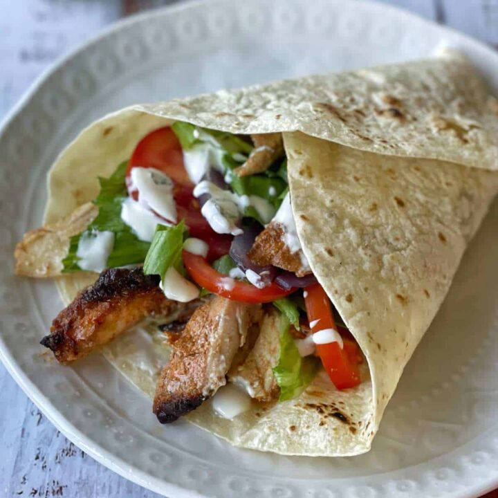 A close up of an assembled chicken gyros on a white dinner plate.