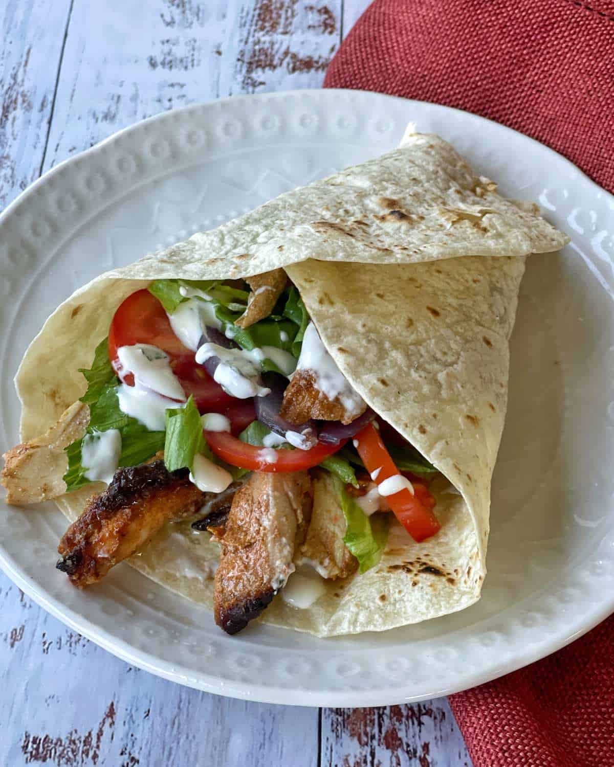 A close-up of a made chicken gyro on a white plate.  