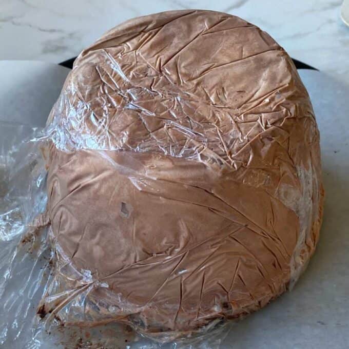 The inside of a baked Alaska covered in cling film on a marble bench.