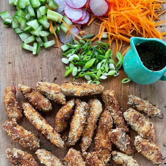 All of the sliced, cooked and combined ingredients for Crispy Coconut Chicken Poke Bowls on a wooden chopping board.