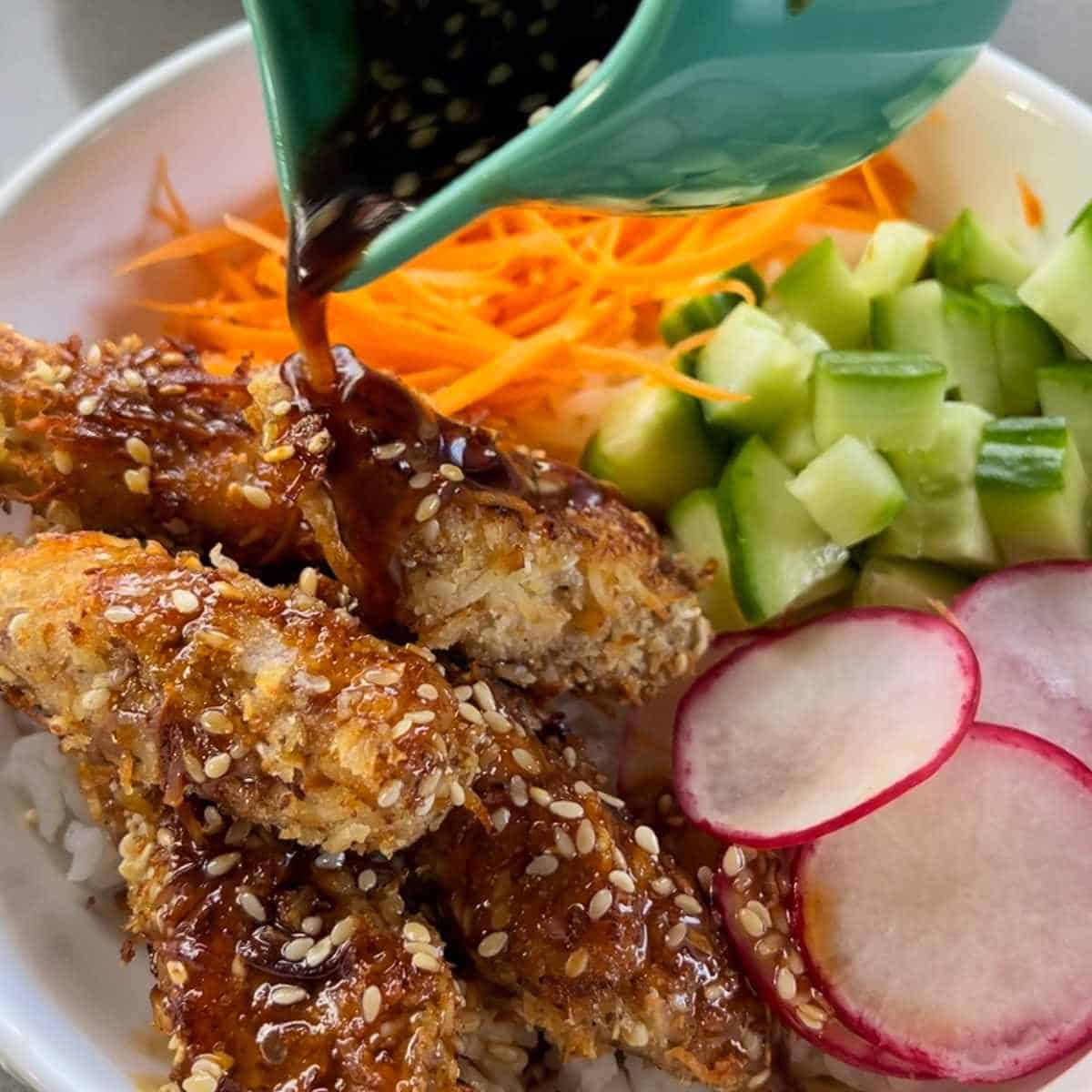 A close up shot of a Crispy Chicken Poke Bowl, sauce is being poured over the top of the crumbed chicken pieces.