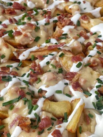 Loaded Hot Chips served in a lined tray with sour cream, crispy bacon pieces and sliced chives over the top.