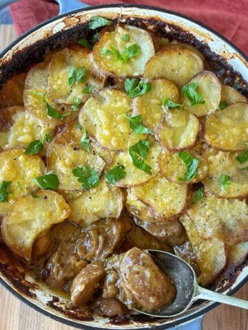 Bird's eye view of a cooked potato and sausage pie in a large casserole dish with a spoon scooping some of the filling out.