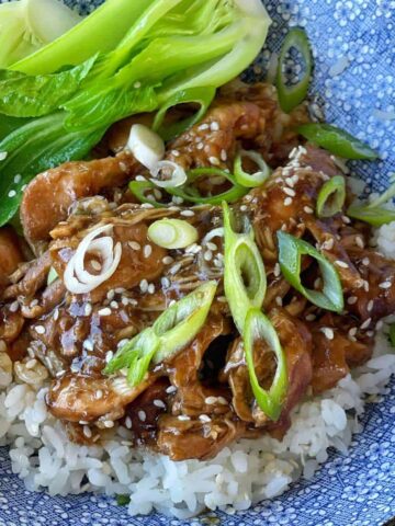 Honey Soy Chicken served over rice in a blue bowl with bok choiy and sliced spring onion and sesame seeds scattered over the top.
