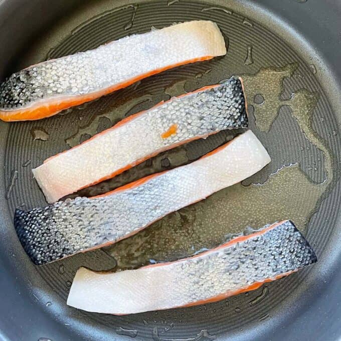 Four salmon fillets frying in a frypan.