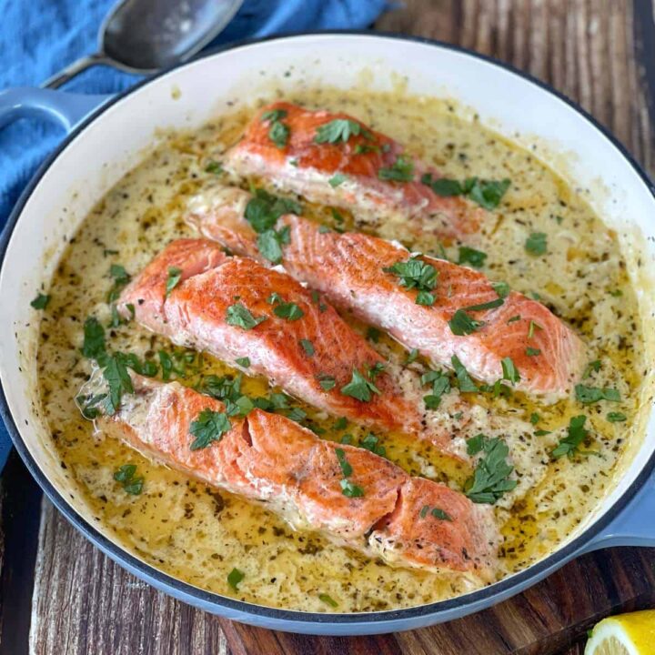 Cooked Creamy Salmon fillets in a round ceramic dish sitting on a wooden chopping board