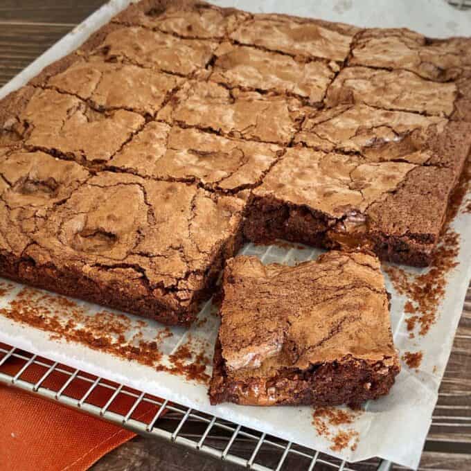 Cooked and slice brownie cooling on a baking rack. The corner square has been cut and pulled out to show the gooey filling.