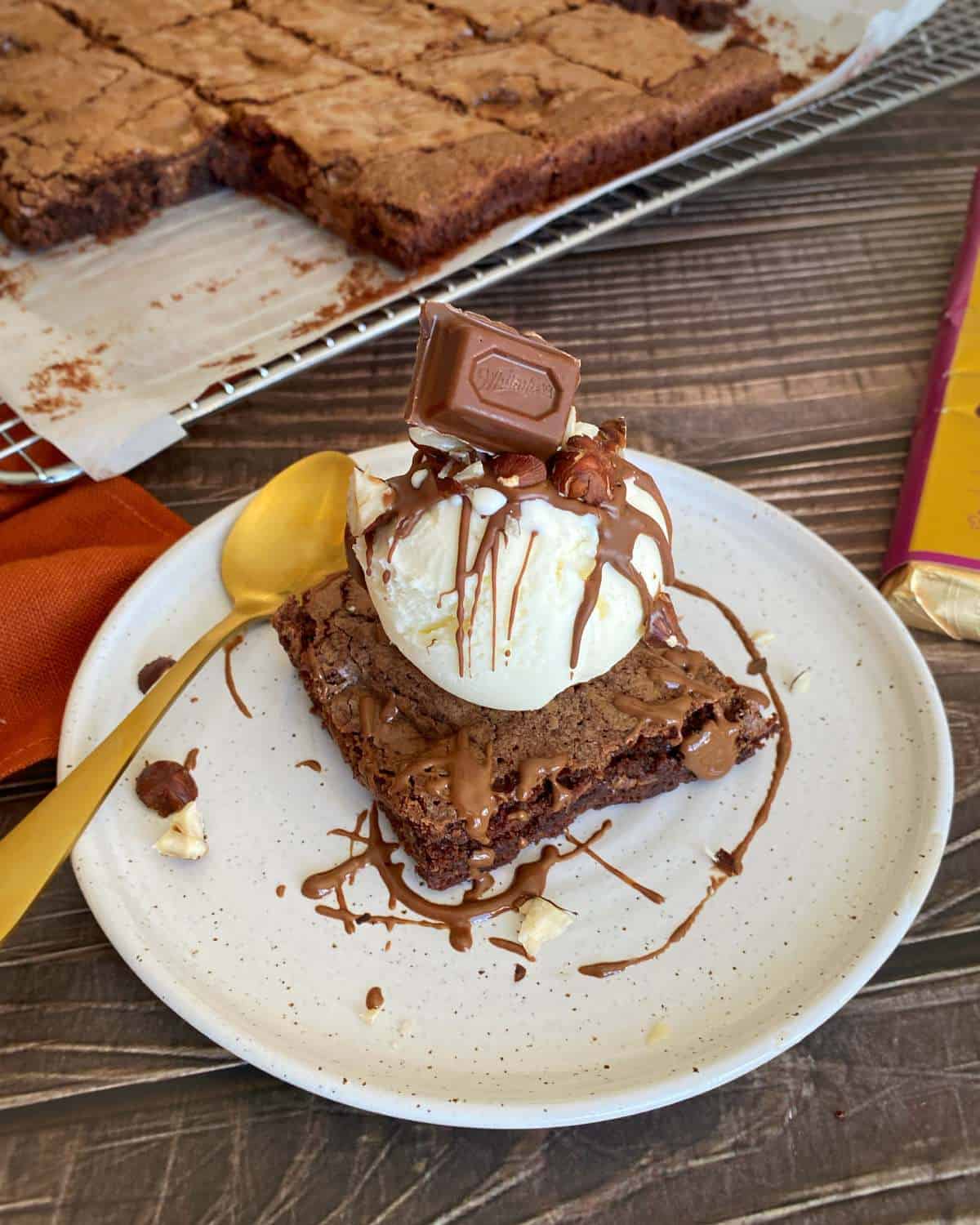 Hazella Brownie Sundae served on a small white plate with a drizzel of melted chocolate poured over the top as well as a square of hazella chocolate.