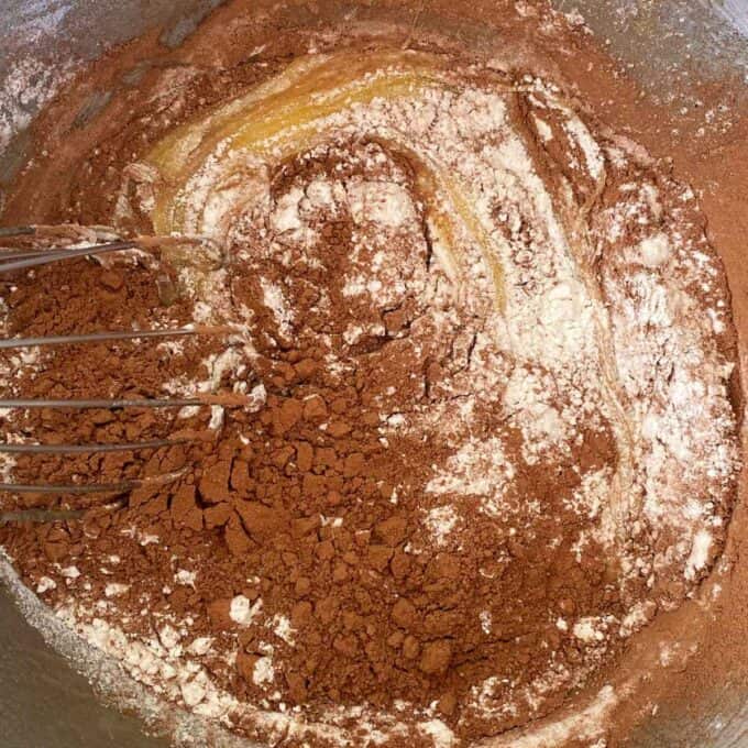 The dry ingredients being added to the wet ingredients to make brownie in a cake mixing bowl.