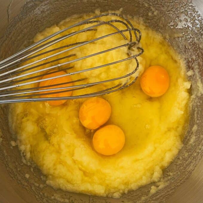 Creamed butter and sugar in a mixing bowl with eggs being added.