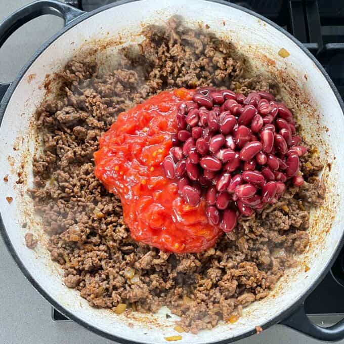 Cooked mince in a frying pan with tomatoes and red kidney beans on top.