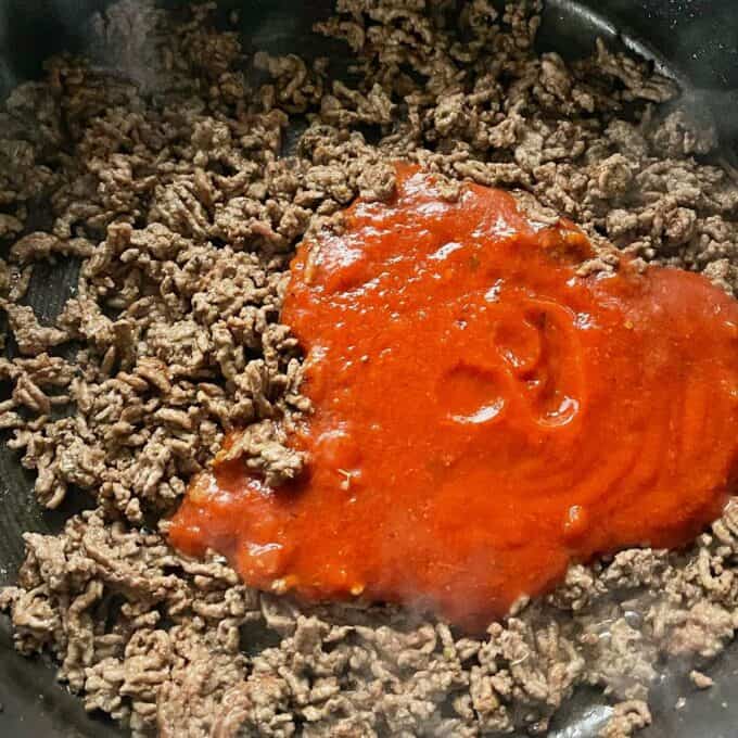 Pasta sauce being added to fried mince and spices in a frypan.