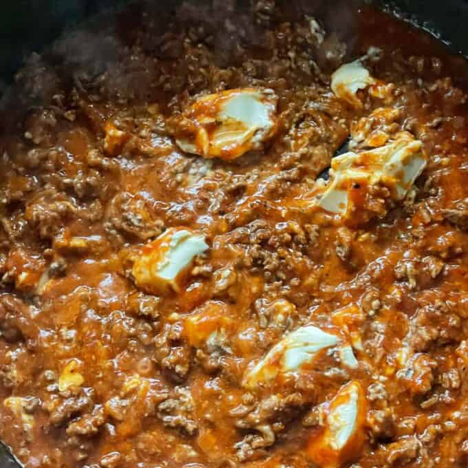 Cream cheese being added to pasta sauce, mince and spices in a medium sized frypan.