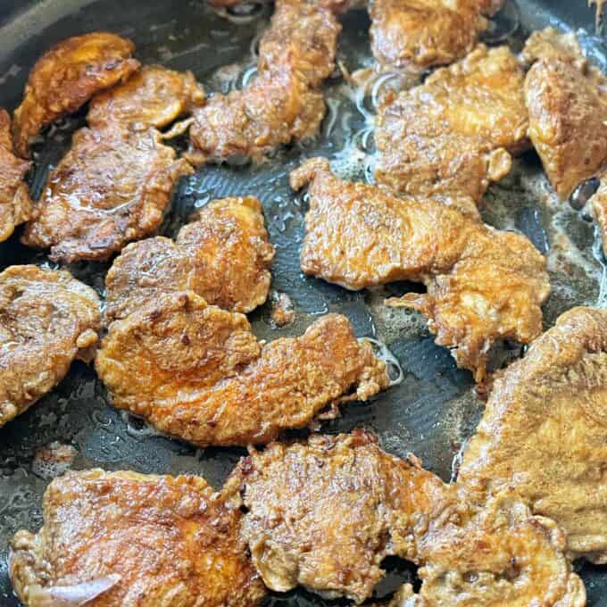 Chicken pieces frying in a fypan.