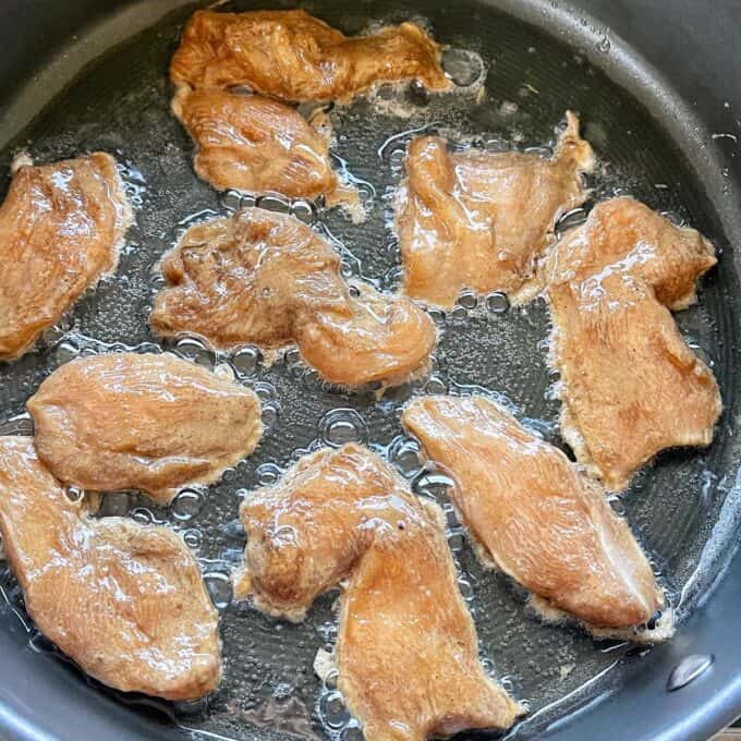 Marinated chicken pieces frying in a frypan.