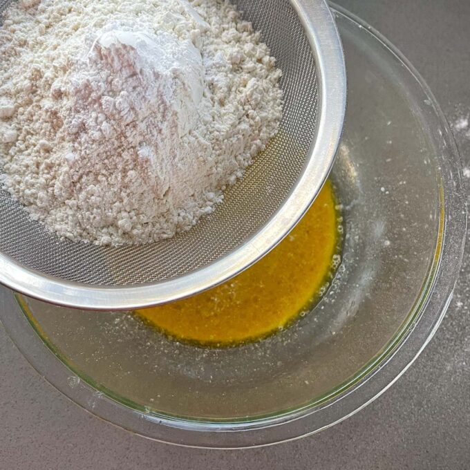 Flour being sifted into melted butter and godlen syrup in a glass bowl.