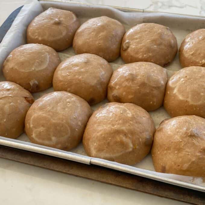 Rolled hot cross dough buns sitting on a lined baking tray.