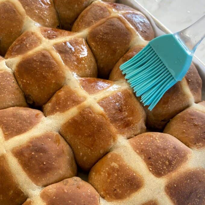 Cooked Hot Cross Buns being brushed with the glaze.