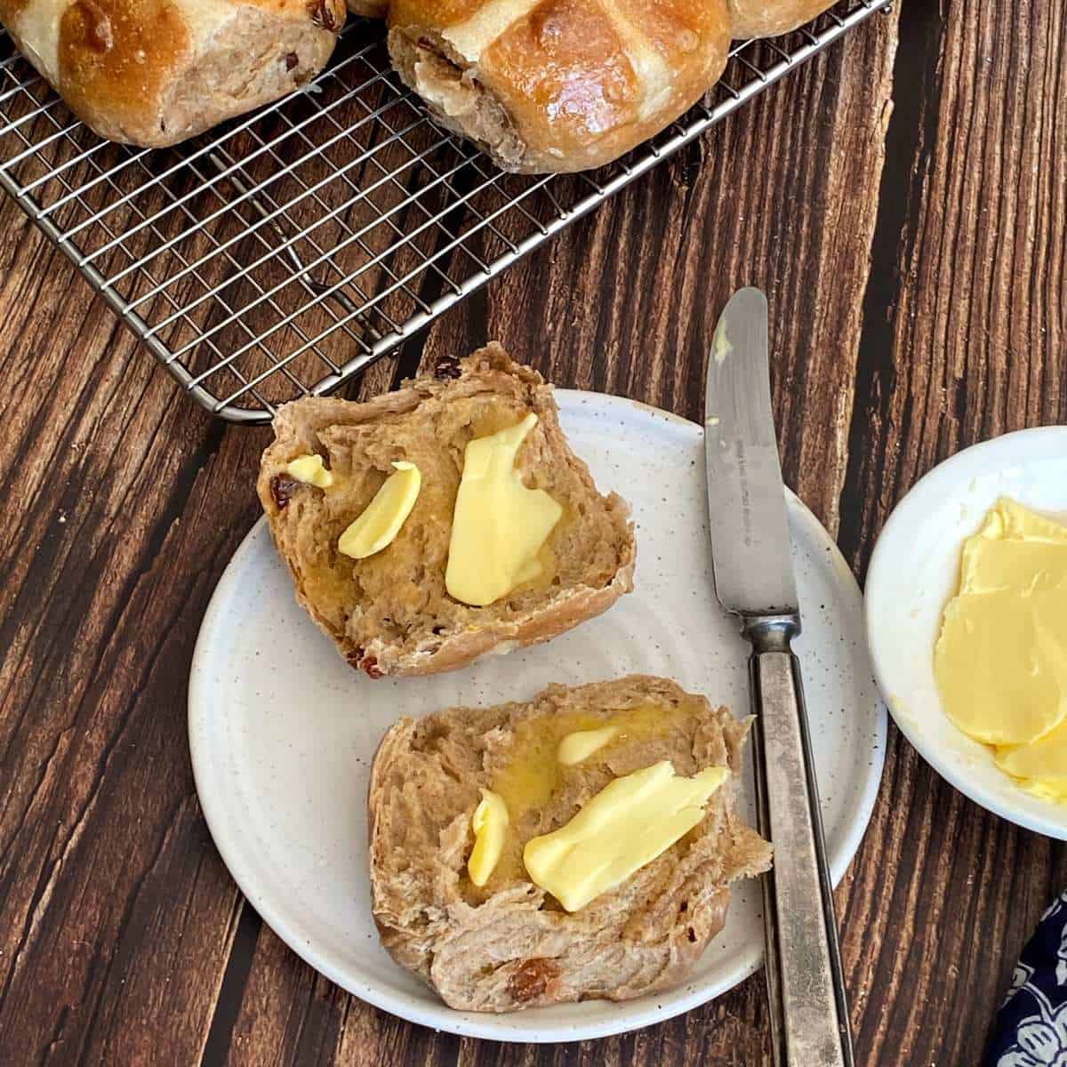 One sliced hot cross bun on a white plate served with butter.