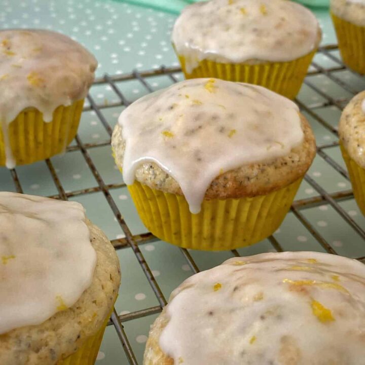 A close up of iced lemon poppyseed muffins on a baking rack.