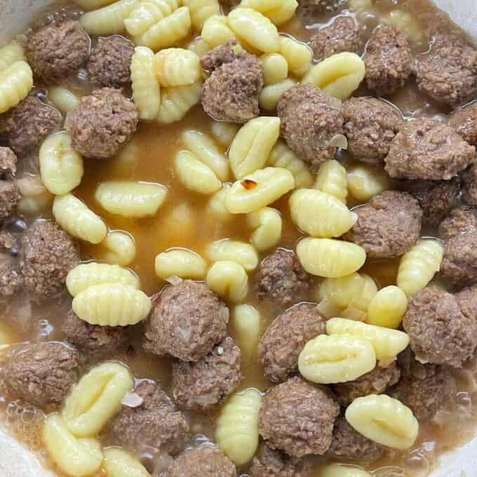 Meatballs, gnocchi, onion and beef stock simmering in a ceramic dish.