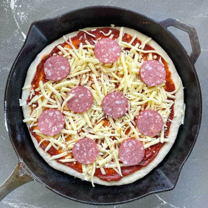 An assembled but uncooked pepperoni pizza in a deep skillet frypan.