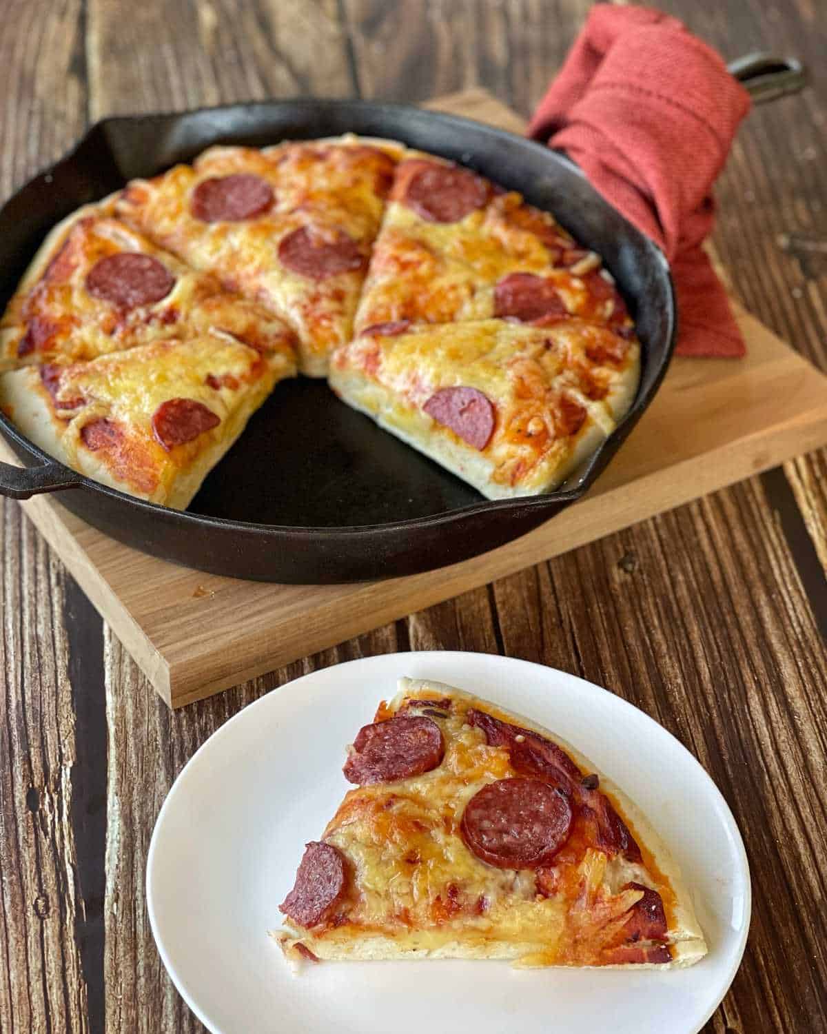 A close up picture of a cooked deep skillet pepperoni pizza, sliced and one slice removed and served on a white plate.