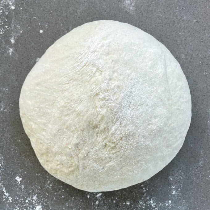 A ball of pizza dough sitting on a grey bench top